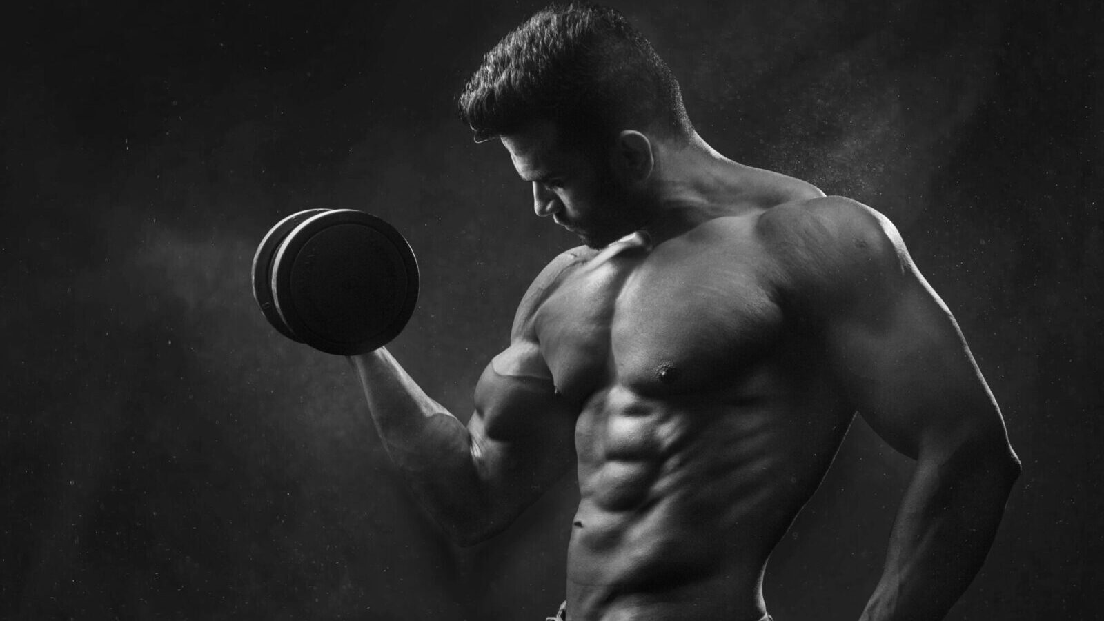 Powerful black and white portrait of a shirtless bodybuilder lifting dumbbells in the gym.