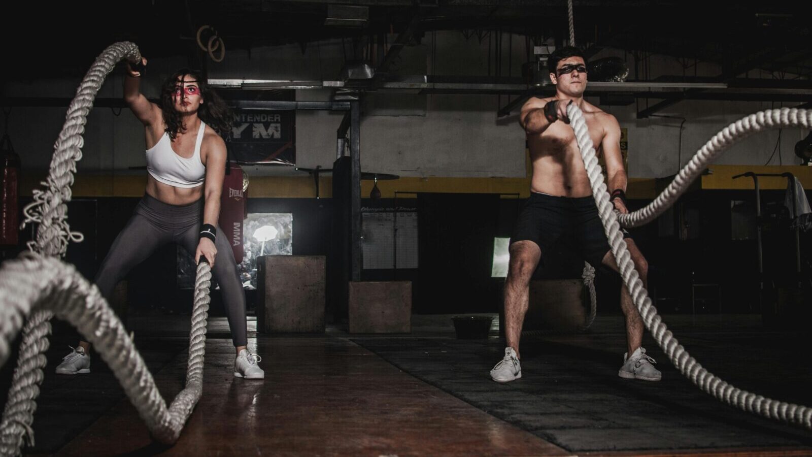 Dos personas participan en un poderoso entrenamiento con cuerdas de batalla en interiores, mostrando fuerza y energía.
