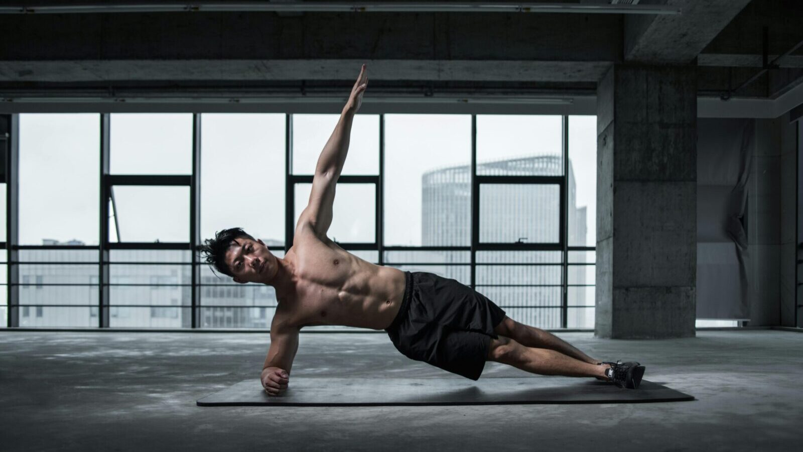 Fit man doing a side plank in an urban indoor gym, showcasing core strength and balance.