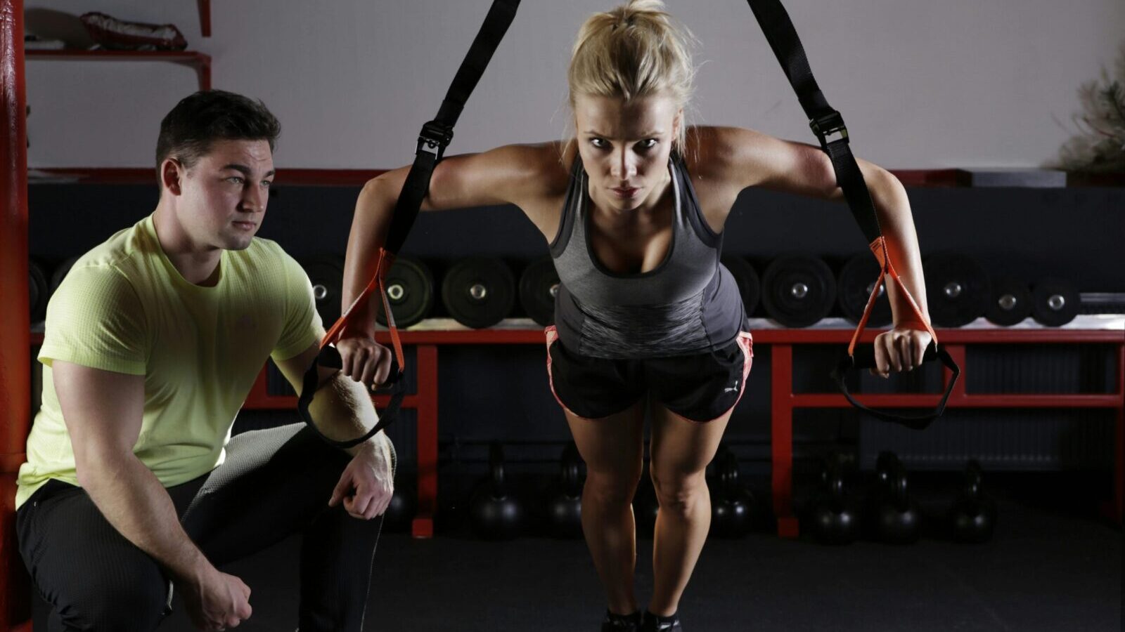 A woman performing strength training with a trainer in a gym setting, showcasing fitness and dedication.